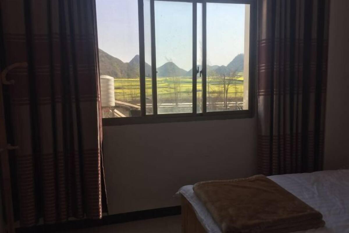 A room with a bed, a window with curtains, and a view of a mountainous landscape.