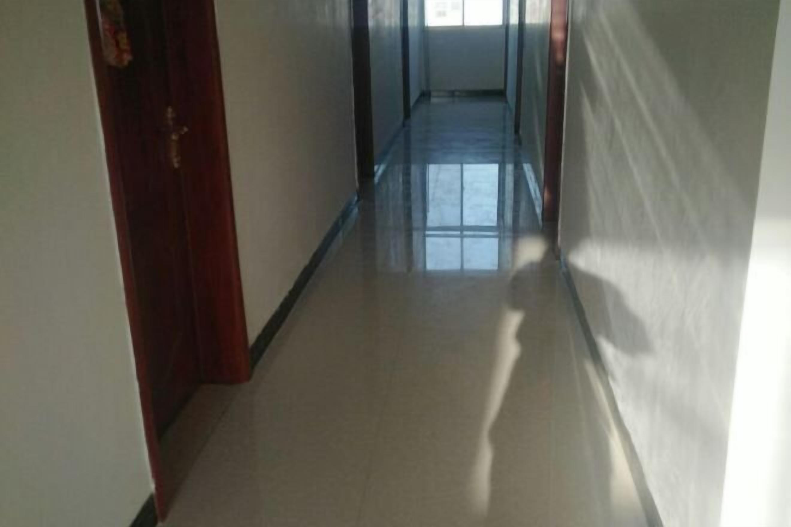 Un pasillo estrecho y bien iluminado con piso reflectante que conduce a una puerta al final.