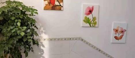 Una escalera con una planta en maceta a la izquierda y tres cuadros con motivos florales en la pared.