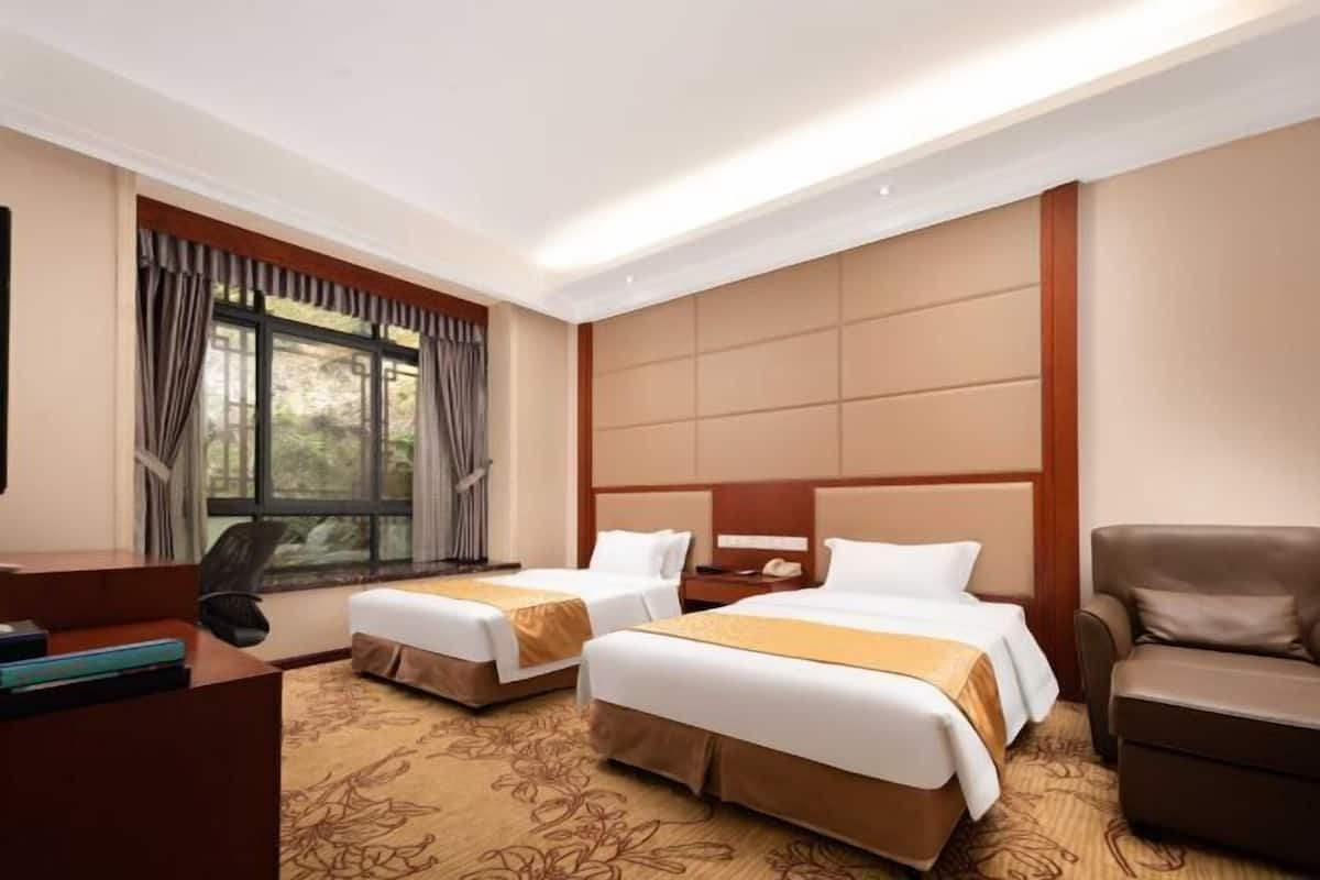 A hotel room with two beds, a desk, a chair, and a large window with curtains.