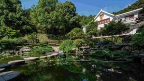 Un edificio tradicional japonés con un estanque de carpas y abundante vegetación.