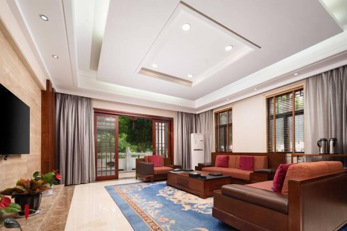 A spacious living room with a large sofa set, a coffee table, and a TV mounted on the wall.