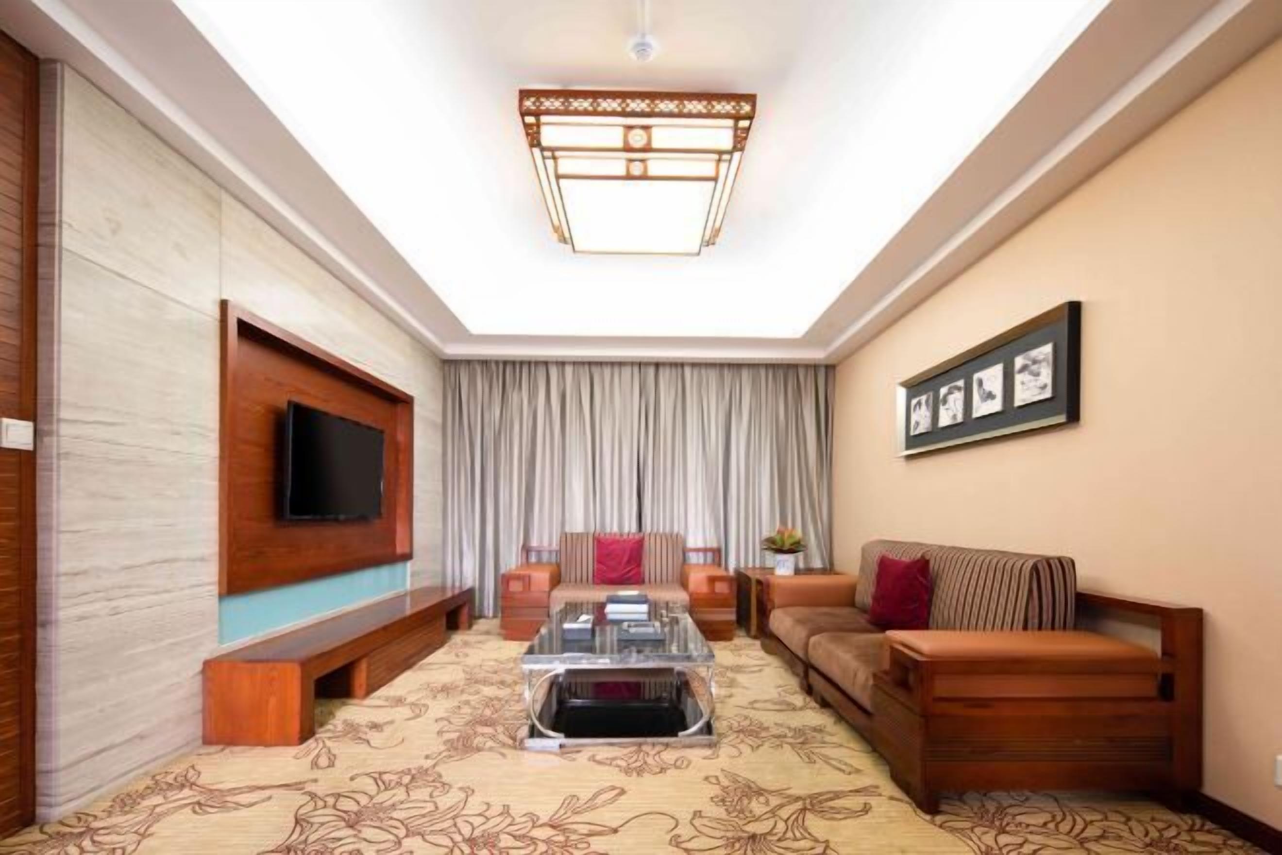 A living room with a flat-screen TV mounted on the wall, a sofa, a coffee table, and a patterned carpet.