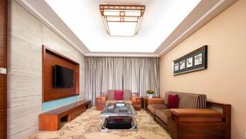 A living room with a flat-screen TV mounted on the wall, a sofa, a coffee table, and a patterned carpet.