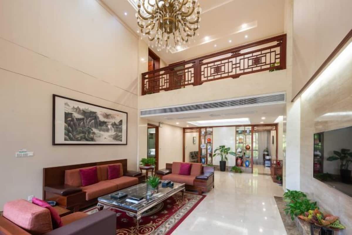 A spacious lobby with a high ceiling, a chandelier, a large framed artwork, and a seating area with sofas and a coffee table.