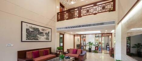 A spacious lobby with a high ceiling, a chandelier, a large framed artwork, and a seating area with sofas and a coffee table.
