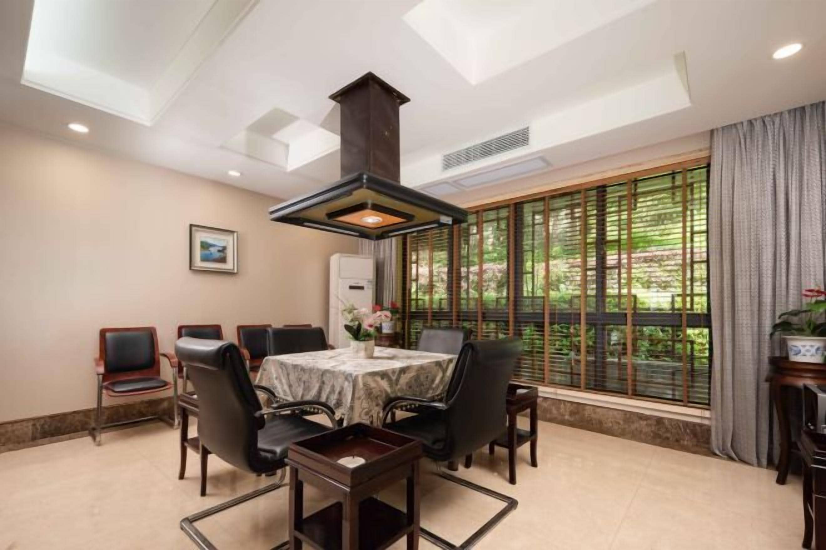 A dining area with a table and chairs, a large window with a view of greenery, and a ceiling light fixture.