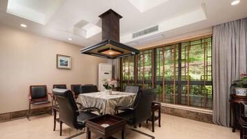A dining area with a table and chairs, a large window with a view of greenery, and a ceiling light fixture.
