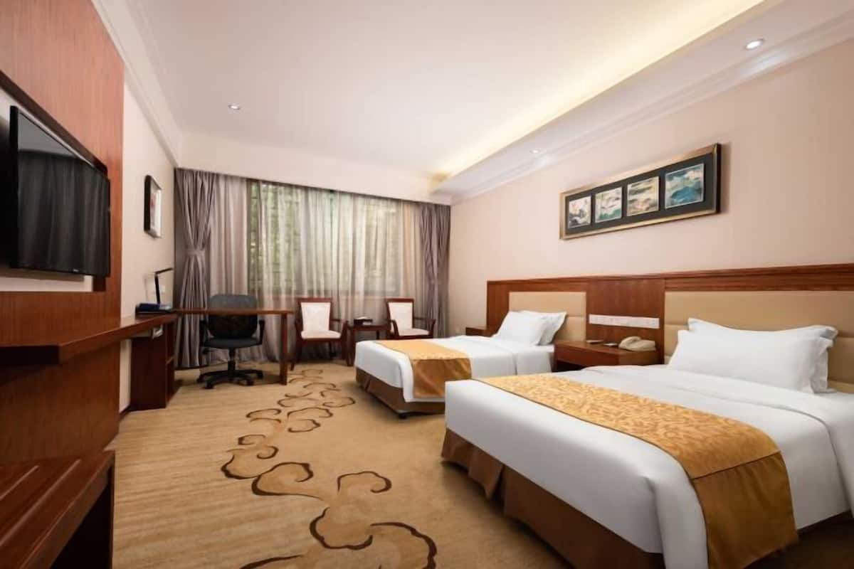 A hotel room with two beds, a desk, a television, and a window with curtains.