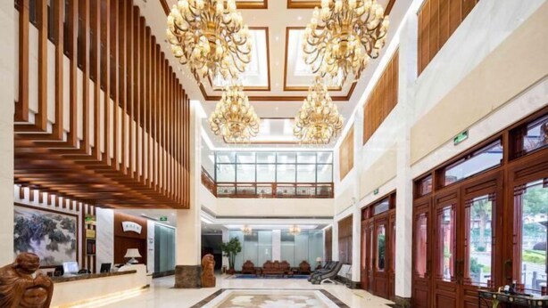 Un vestíbulo amplio con techo alto, candelabros ornamentales, un mostrador de recepción y un área de estar.