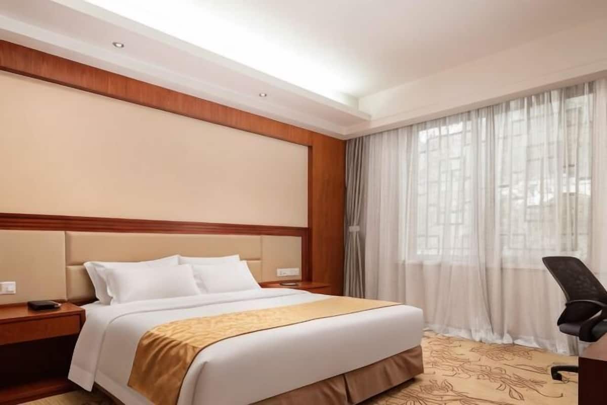 A hotel room with a bed, a desk, a chair, and a large window with curtains.