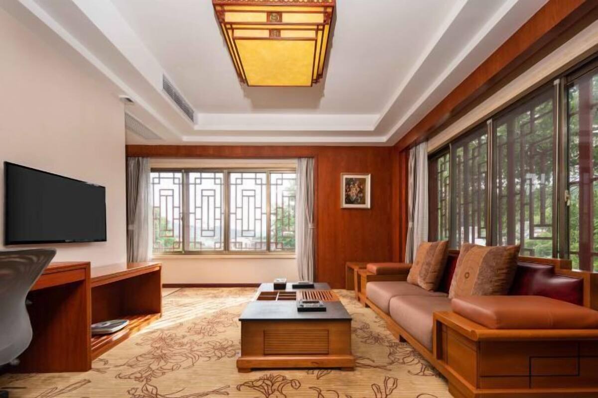 A living room with a sofa, a coffee table, a TV, and a large window with a view of greenery.