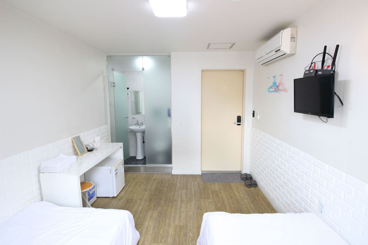 Habitación de hotel con dos camas, un escritorio pequeño, un lavamanos y un televisor montado en la pared.