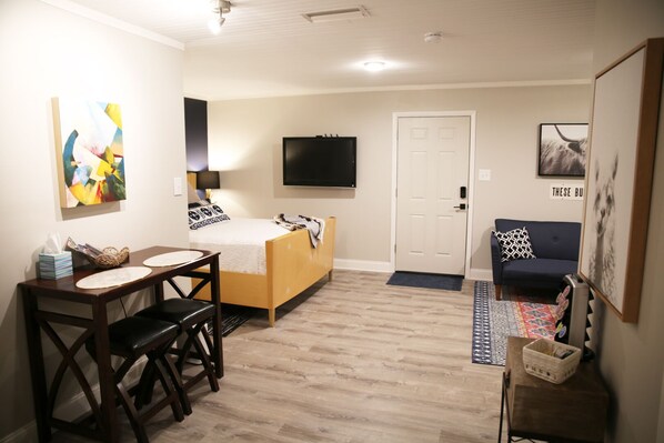 A compact hotel room with a bed, a desk with a chair, a television, a couch, and artwork on the walls. - The Sylvan Suite by Curated Stays: Queen Bed (Abilene)