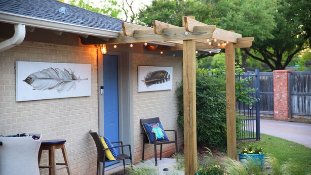 Une maison avec une pergola en bois, deux chaises avec des coussins et une porte bleue.