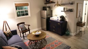 Un espace de vie compact comprenant un canapé, une table basse, un fauteuil et un coin cuisine équipé d’un réfrigérateur, d’un four à micro-ondes et d’un évier.