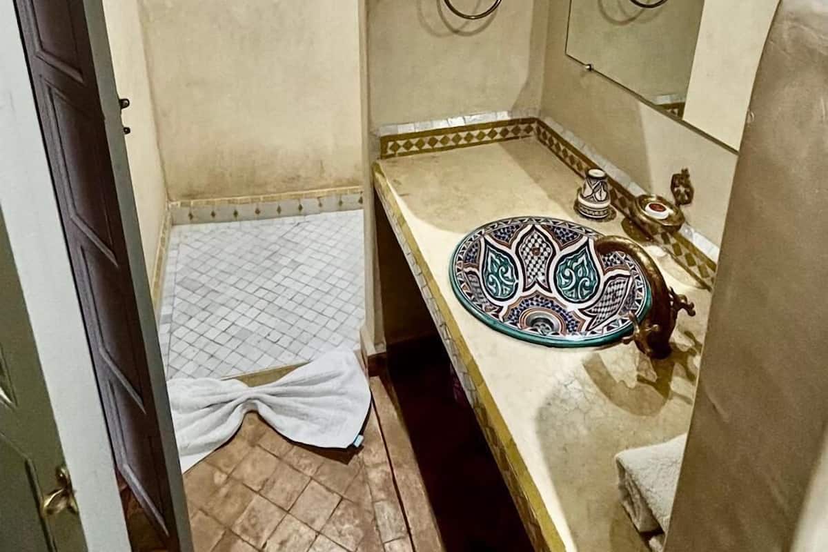 A bathroom with a shower, a sink with a decorative plate, and a towel hanging on the wall.