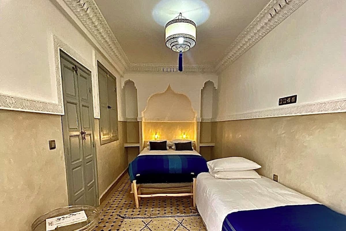 A hotel room with a bed, a small table, and a decorative ceiling light.