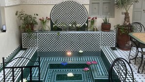 A courtyard with patterned tiles, a round table, chairs, potted plants, and a decorative wall. - RIAD MAGNOLIA (Marrakech)