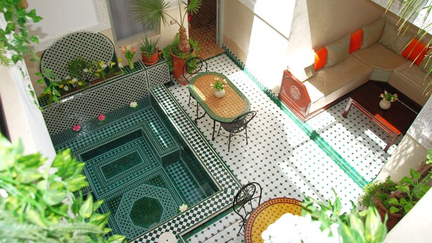 A small courtyard with a checkered floor, a round table with chairs, a sofa with cushions, and potted plants. - RIAD MAGNOLIA (Marrakech)