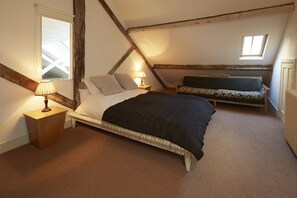A bedroom with a bed, a nightstand, a lamp, a sofa, and a skylight.