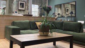 A spacious living room with a green sofa, a wooden coffee table, and a large window allowing natural light. - Extremely spacious loft located in the vibrant America Ground close to the beach (Hastings)