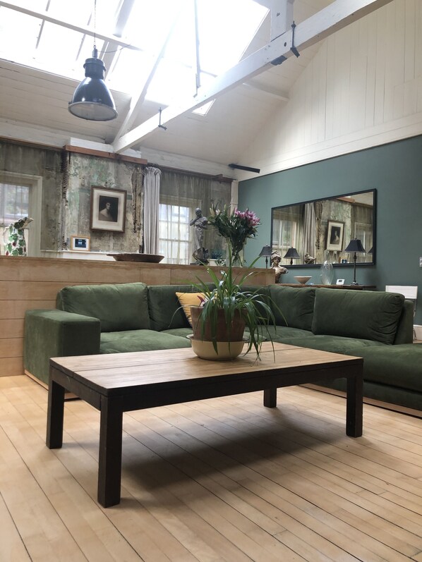 A spacious living room with a green sofa, a wooden coffee table, and a large window allowing natural light.