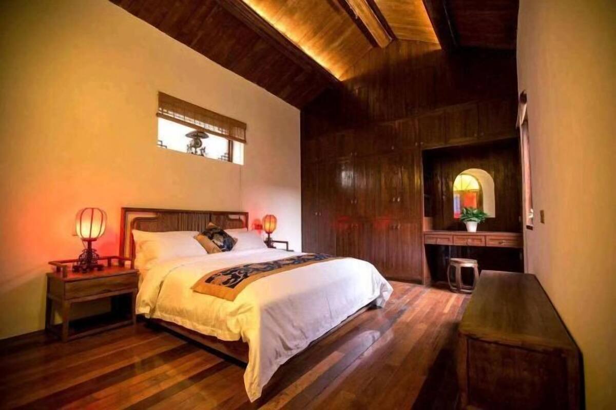 Un dormitorio con techo de madera, una cama con ropa blanca, una mesita de noche con lámpara y un banco de madera.