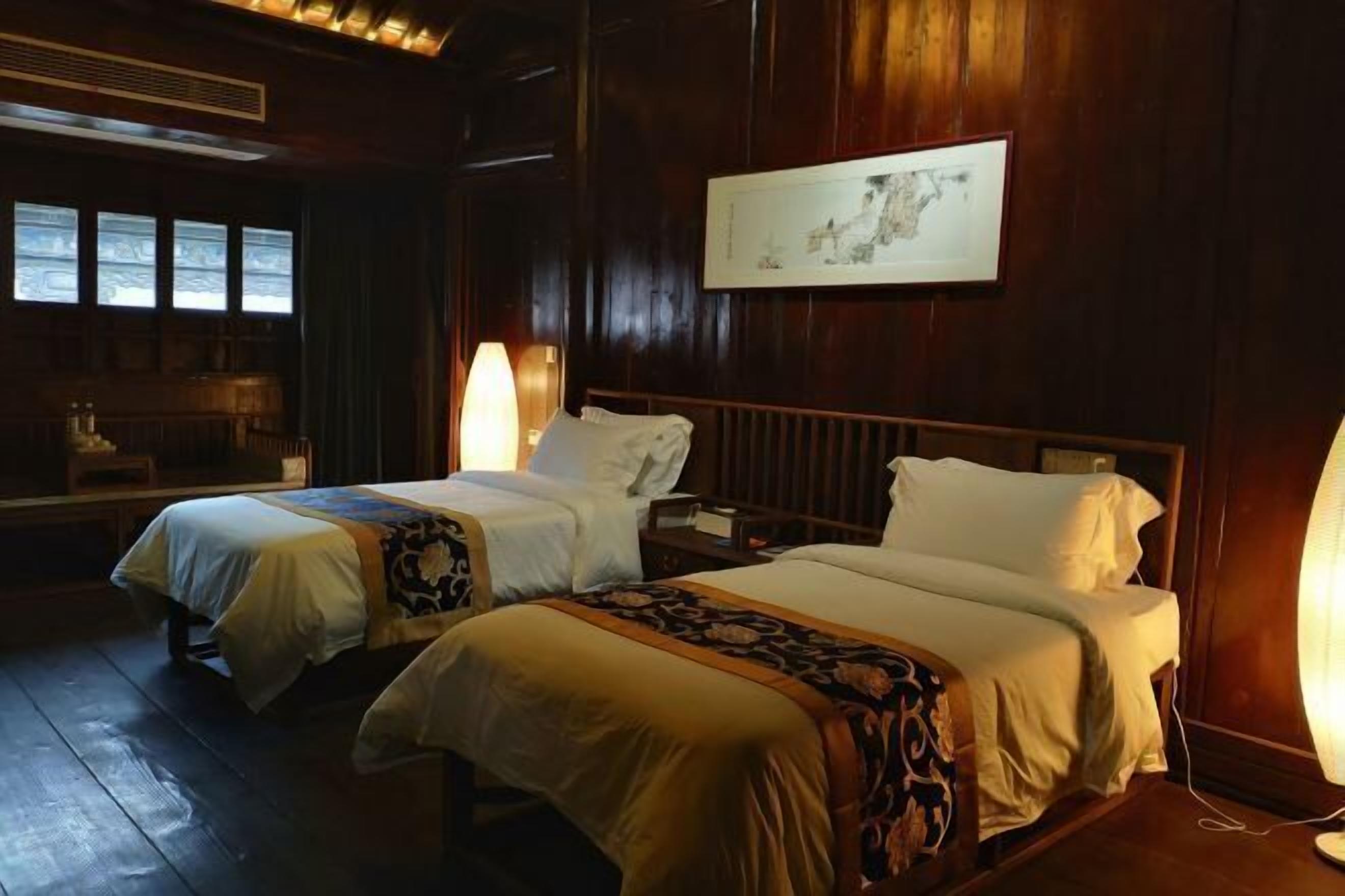 A hotel room with two beds, wooden walls, a framed picture, and a window with blinds.