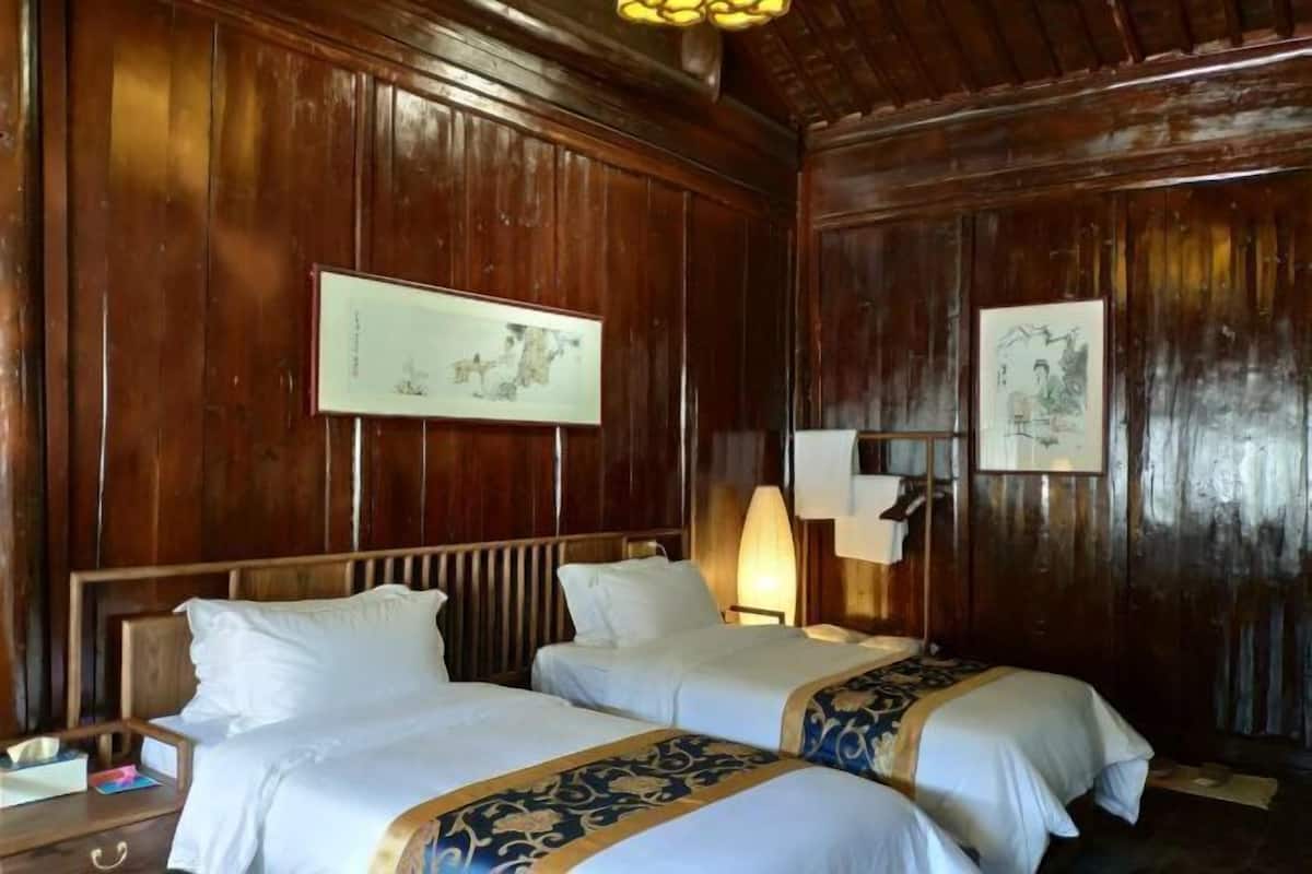 Una habitación con paneles de madera, dos camas con sábanas blancas, una mesita de noche, una lámpara y dos cuadros en la pared.