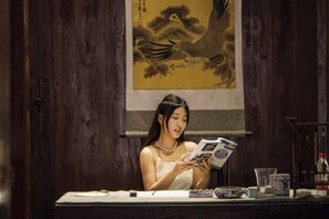A person seated at a table with a book, a glass, and a bottle. - Hanqing Hostel (Deqing)