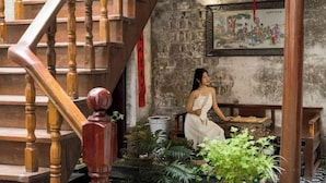 A staircase with wooden balusters, a seated person on a bench, and a wall with a framed painting. - Hanqing Hostel (Deqing)