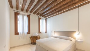 Une chambre avec un plafond en bois, un lit avec une tête de lit, une table de chevet avec une lampe et deux fenêtres avec des rideaux.