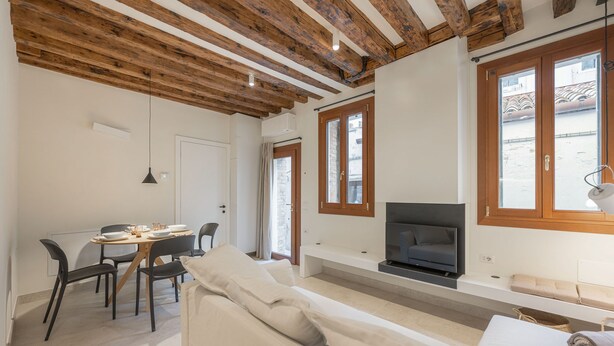 Un salon moderne avec un plafond en bois, un téléviseur, un canapé et un coin repas comprenant des chaises et une table.