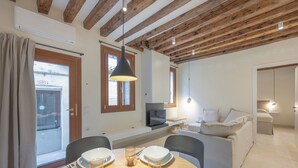 Un salon moderne comprenant un coin repas, des poutres apparentes en bois au plafond, un téléviseur et un canapé.