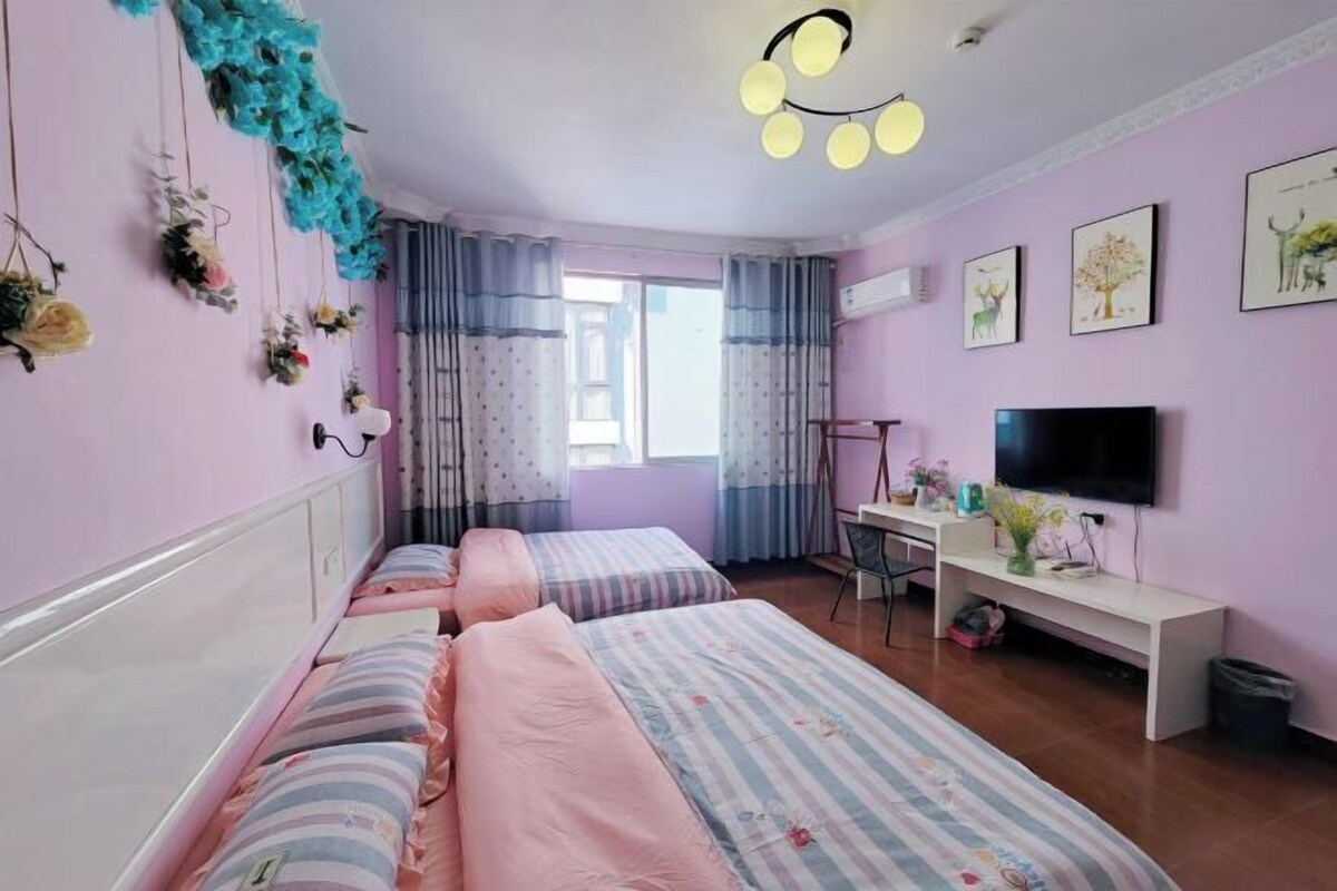 Ein Schlafzimmer mit zwei Betten, einem Schreibtisch, einem Fernseher und einem Fenster mit Vorhängen.
