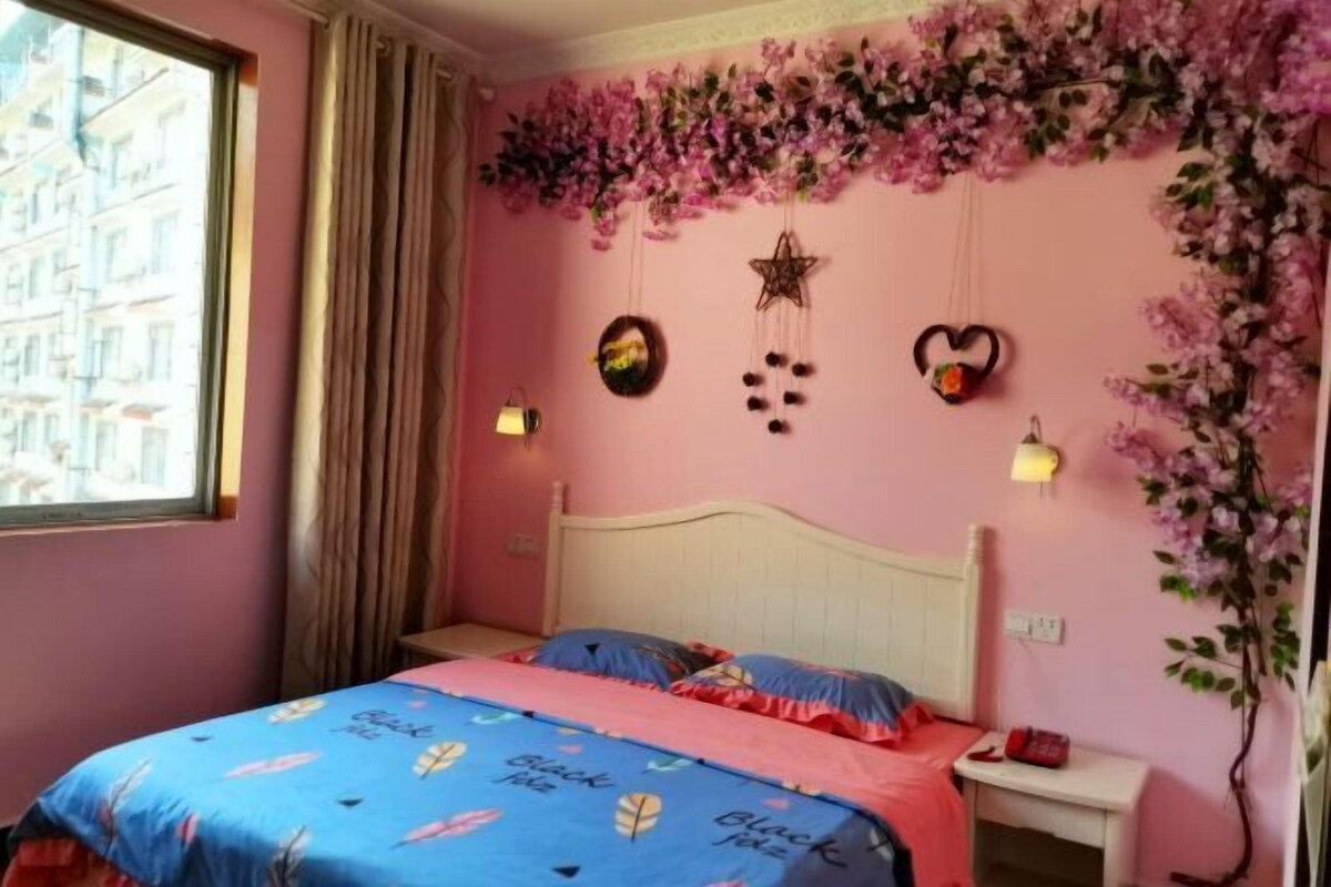Ein Schlafzimmer mit einem Bett, einem Nachttisch, einer Wandlampe und einem Fenster mit Vorhängen.