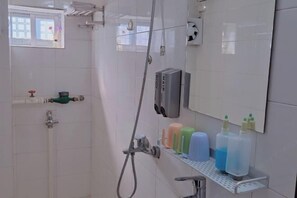 Ein Badezimmer mit Dusche, Toilette, Waschbecken und Spiegel. Auf einem Regal stehen Pflegeprodukte.