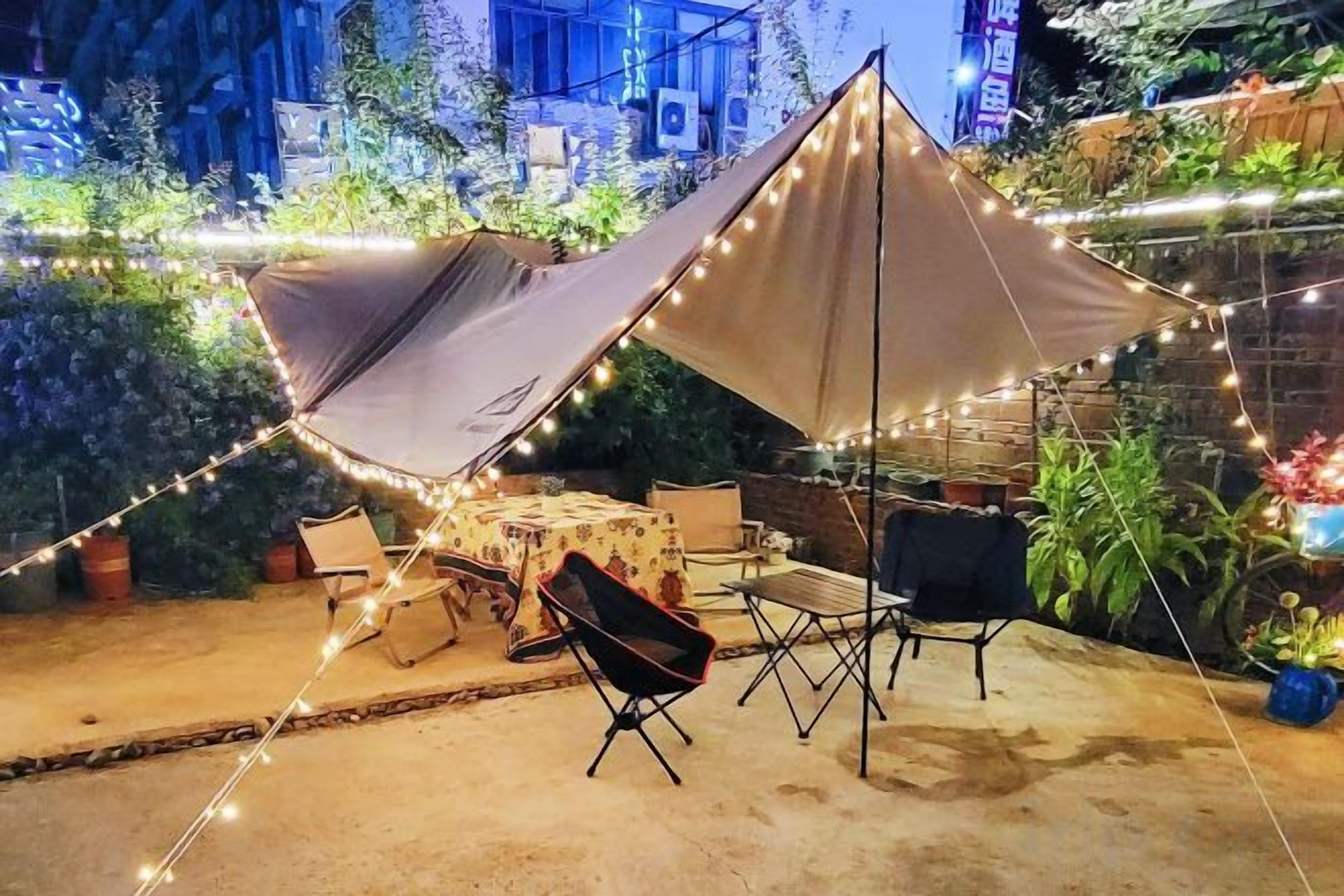 Terrassa exterior amb una gran tenda, llums enfilades i una taula amb cadires.