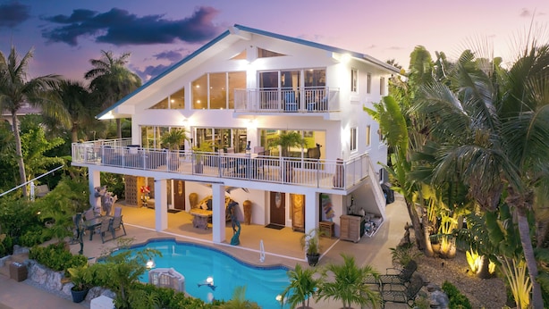 A two-story house with a swimming pool, surrounded by tropical plants and palm trees. - Sleeps 10 - Private house with 110’ of Deep Water Dockage, Pool, Hot Tub & more! (Marathon)