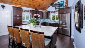 A kitchen with dark wooden cabinets, a large island with a marble countertop, and a stainless steel refrigerator. - Sleeps 10 - Private house with 110’ of Deep Water Dockage, Pool, Hot Tub & more! (Marathon)
