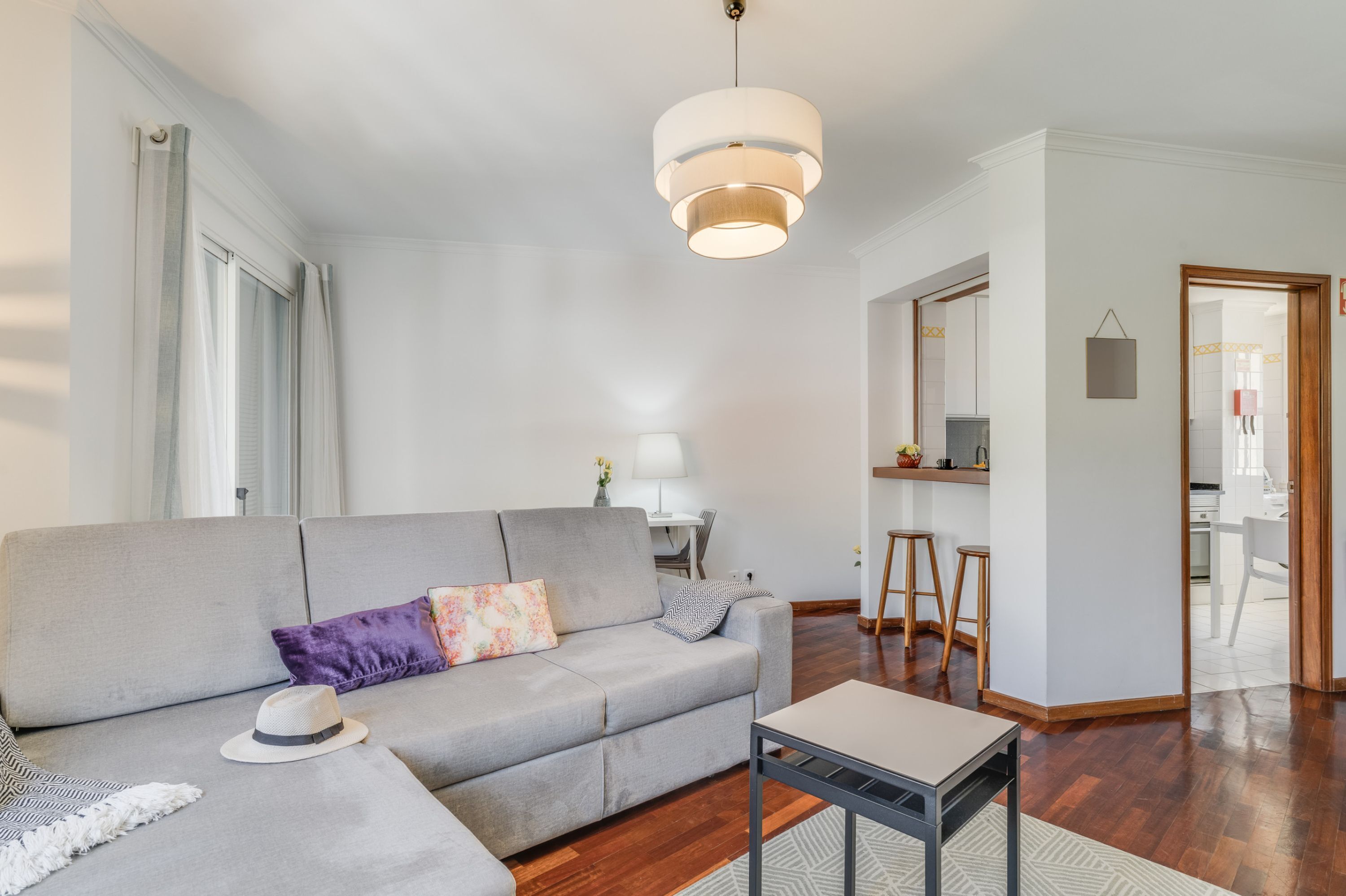 A modern living room with a grey sofa, a small table, and a hanging light fixture.