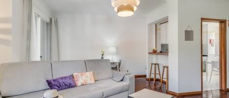 A modern living room with a grey sofa, a small table, and a hanging light fixture.