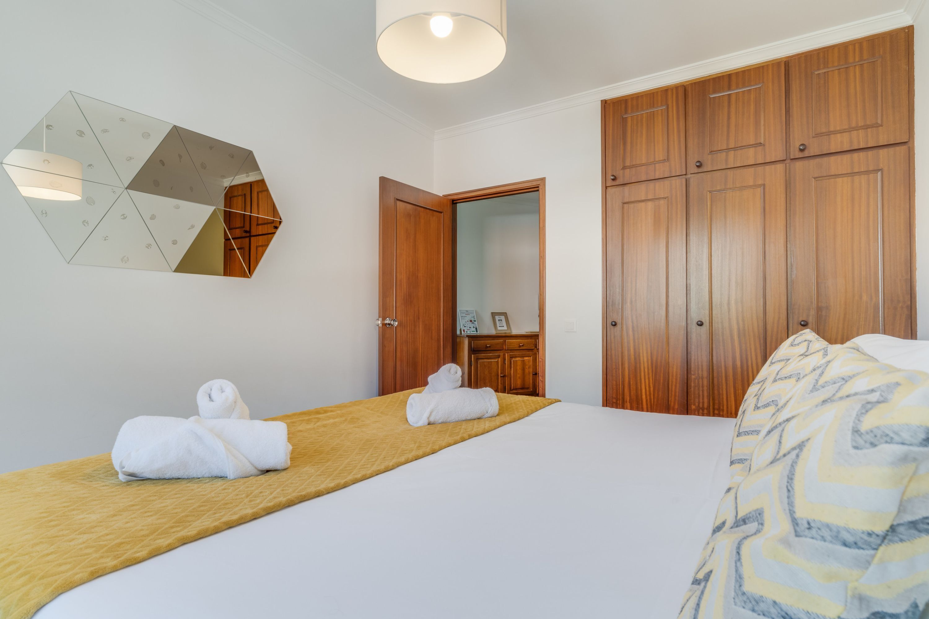 Hotellihuone, jossa on sänky, puinen vaatekaappi, peili ja geometrisesti kuvioitu seinäkoriste.
