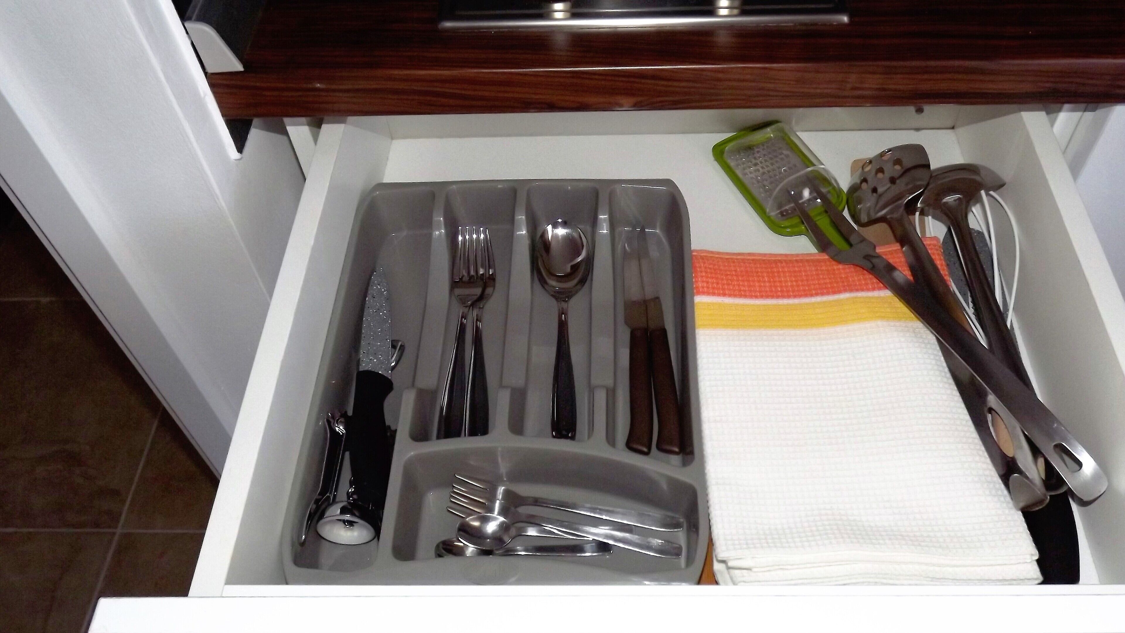 A drawer with neatly organized kitchen utensils including forks, spoons, knives, and a grater.