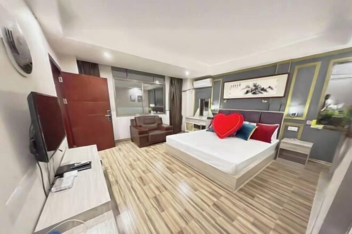 A modern hotel room with a large bed, a desk, a chair, a TV, and a wardrobe.