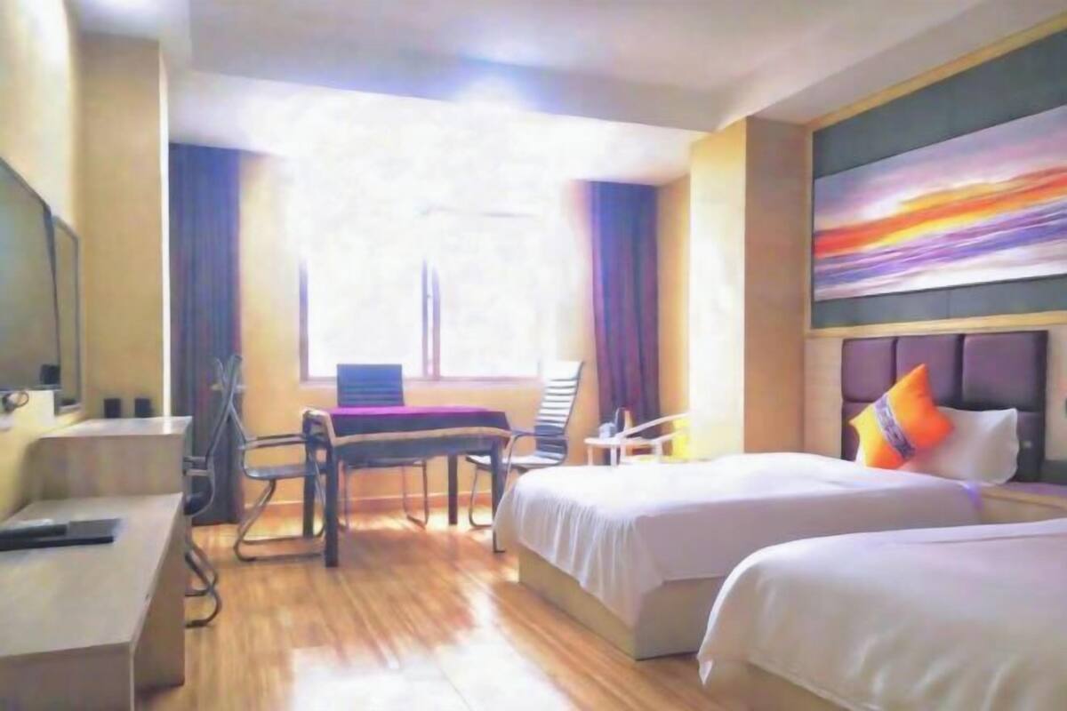 A hotel room with two beds, a desk, a chair, a TV, and a painting on the wall.