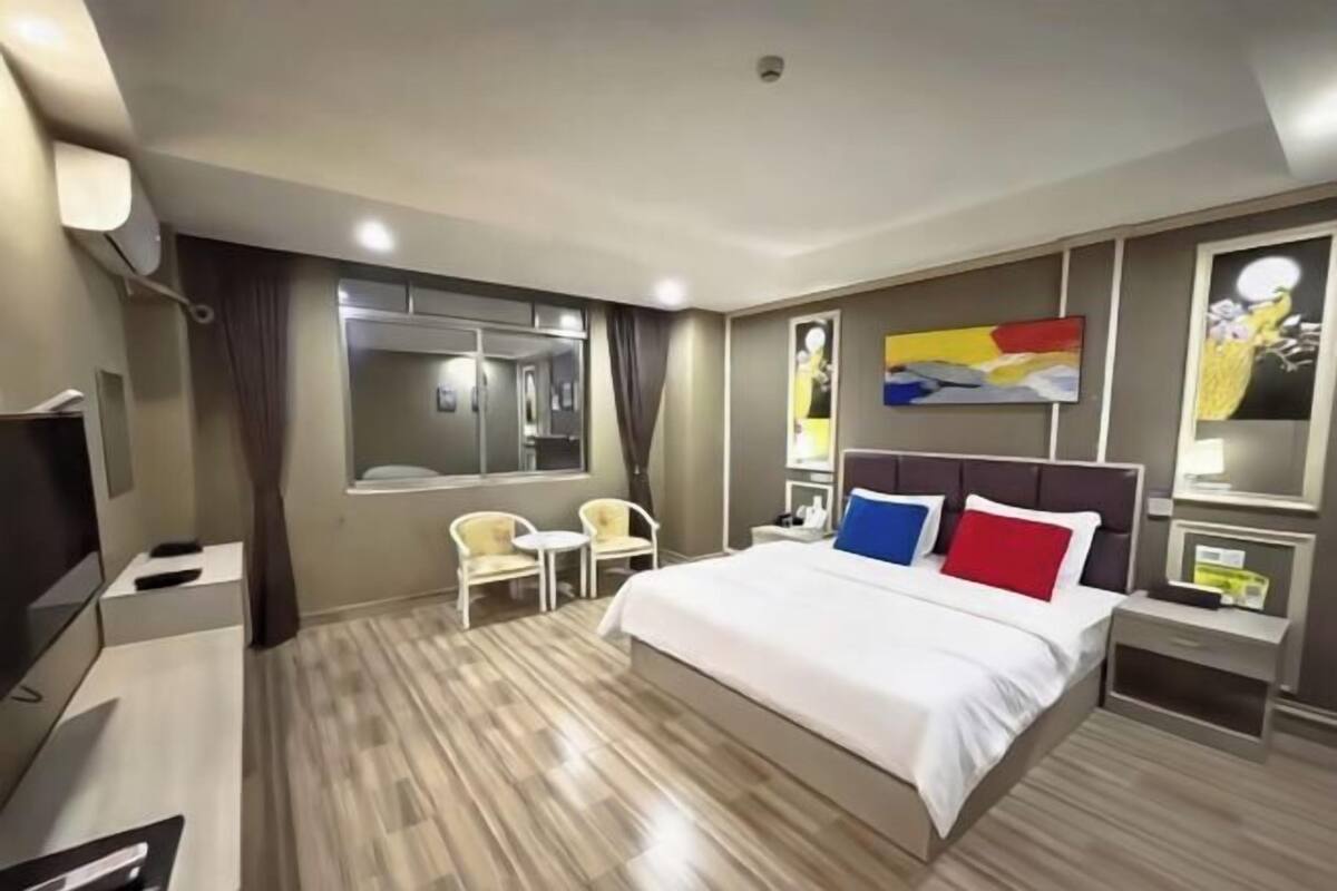 A hotel room with a bed, bedside tables, a TV, a window, and a painting on the wall.