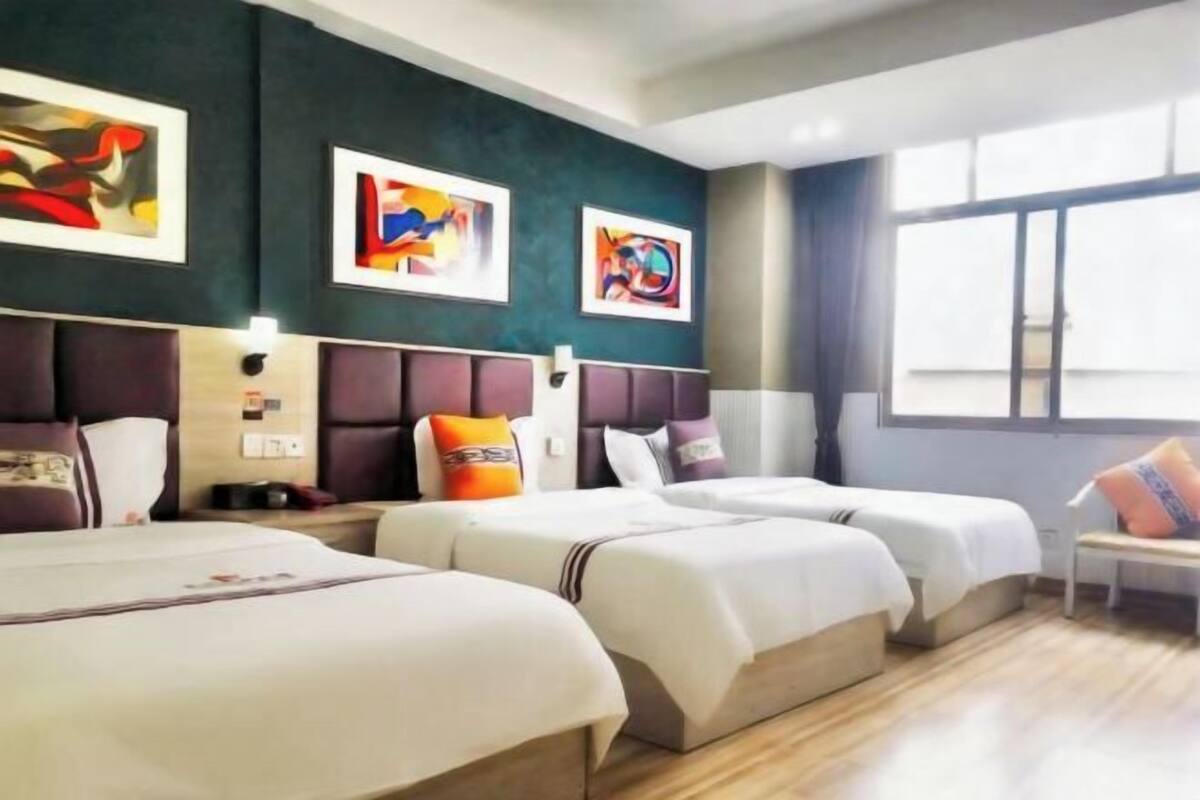 A hotel room with two beds, artwork on the walls, a window with curtains, and a wooden floor.