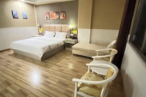 A hotel room with a large bed, a sofa, a small table, and two chairs.